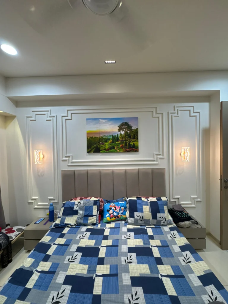 Elegant bedroom interior design featuring wall moulding panels, upholstered headboard, bedside wall lights and modern false ceiling in an Ahmedabad home