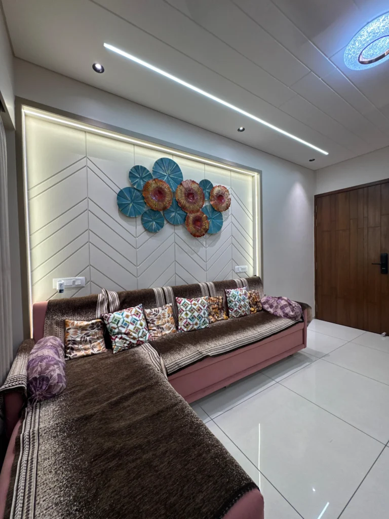 Modern living room interior design featuring decorative wall panelling, ambient LED lighting, false ceiling and comfortable L-shaped sofa in an Ahmedabad home