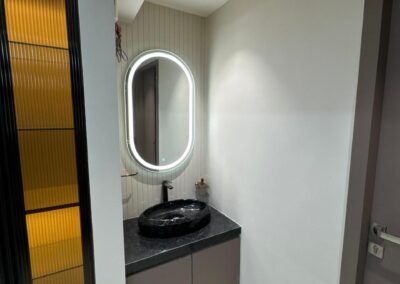 Compact vanity area with backlit mirror, countertop basin, and vertical storage unit