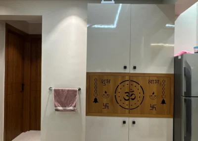 Home mandir unit with carved wooden panel, closed storage cabinets, and clean wall finish