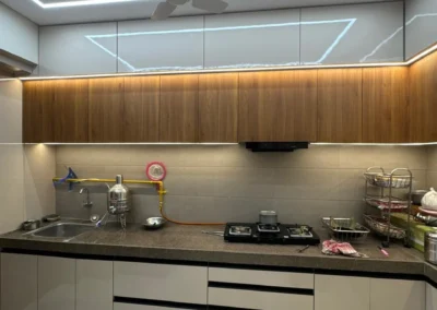 Modular kitchen with laminate cabinets, overhead storage, black countertop, and warm under-cabinet lighting