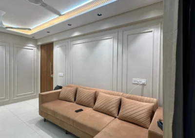 Living room interior with L-shaped sofa, wall paneling, and POP ceiling with concealed lighting
