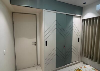 Parents bedroom wardrobe with CNC cut sliding shutters, soft grey finish, and integrated storage designed by J Designs