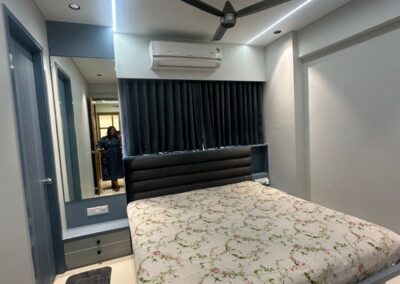 Modern bedroom interior with upholstered headboard, POP ceiling with panel lights, and custom side units designed by J Designs