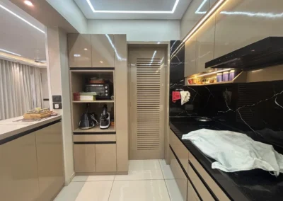 Side view of modular kitchen showing sliding storage door, built-in microwave unit, and tall cabinet design by J Designs