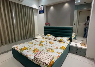 Contemporary bedroom with green upholstered bed, patterned bedding, and full-height curtains designed by J Designs