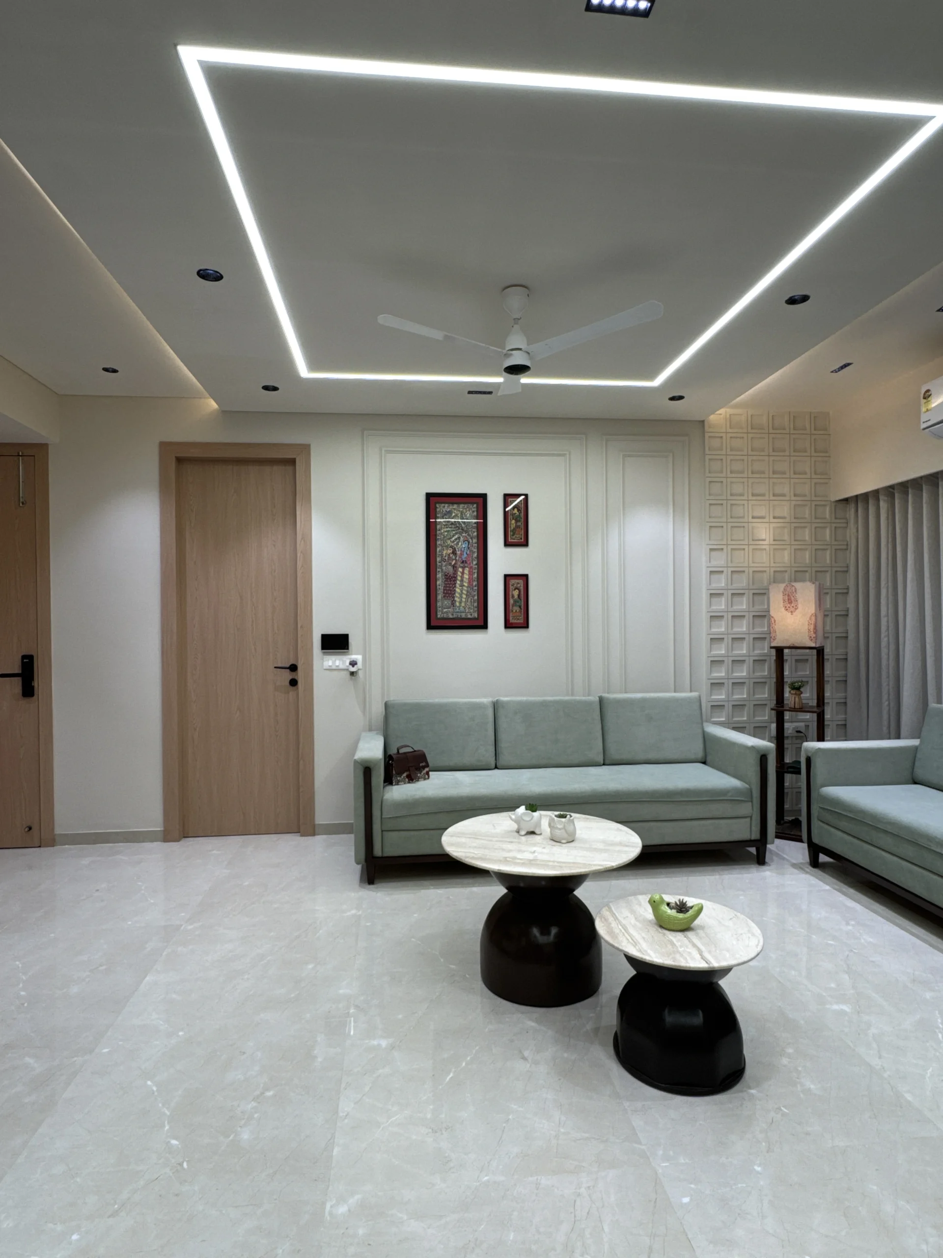 Modern living room interior design in Ahmedabad with linear LED false ceiling, sage green sofa, and geometric wall panel by J Designs